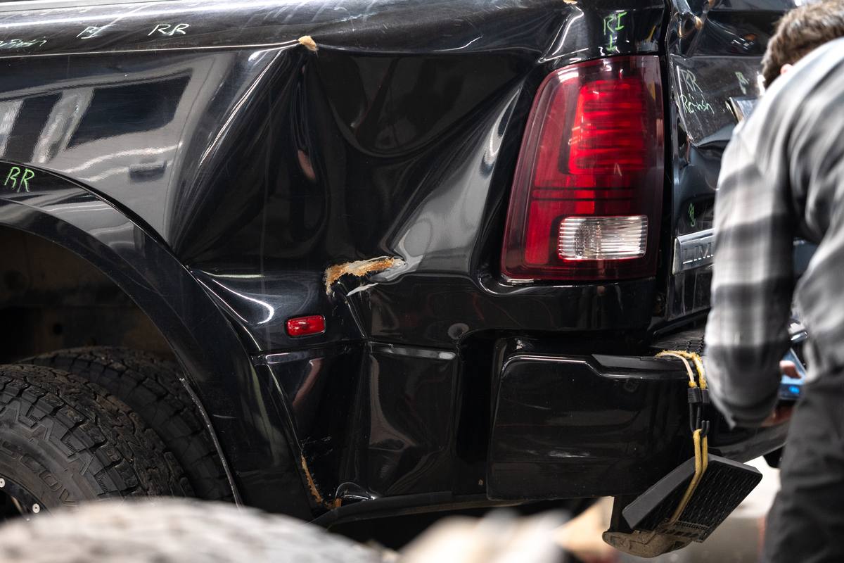 Technician checking collision damage on a black pickup truck at Fix Auto Sherwood North